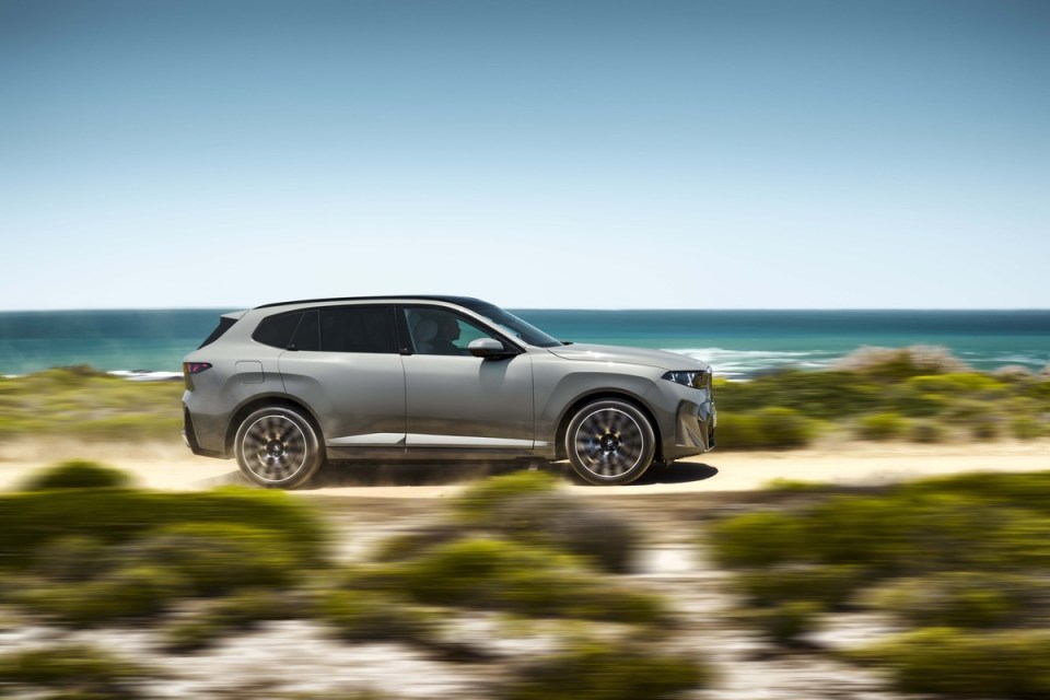 Gray BMW X5 SUV driving on a dirt road beside the ocean under a clear blue sky