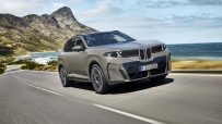BMW X5 driving on a coastal road with mountains and ocean in the background, showcasing its sleek design.