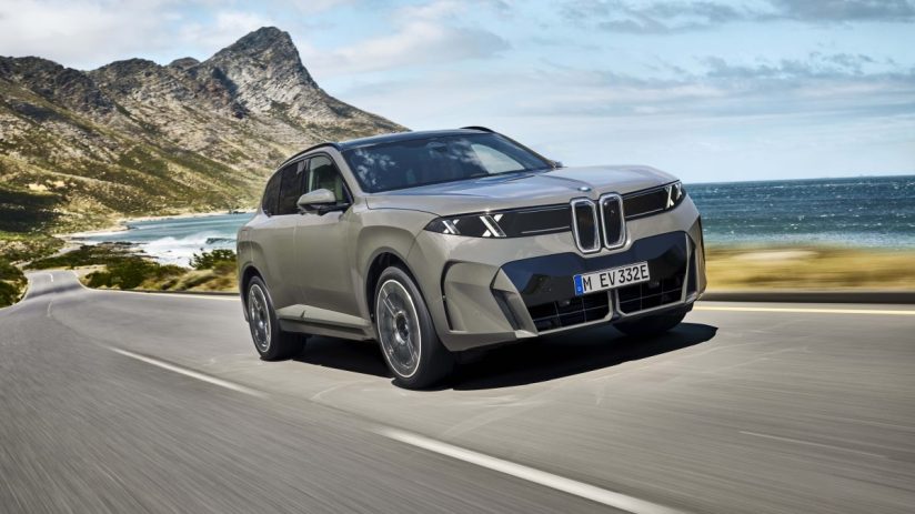 BMW X5 driving on a coastal road with mountains and ocean in the background, showcasing its sleek design.