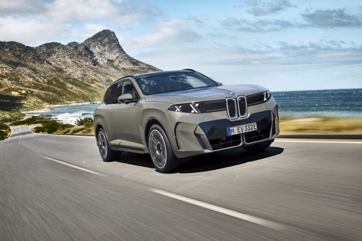 BMW X5 driving on a coastal road with mountains and ocean in the background, showcasing its sleek design.