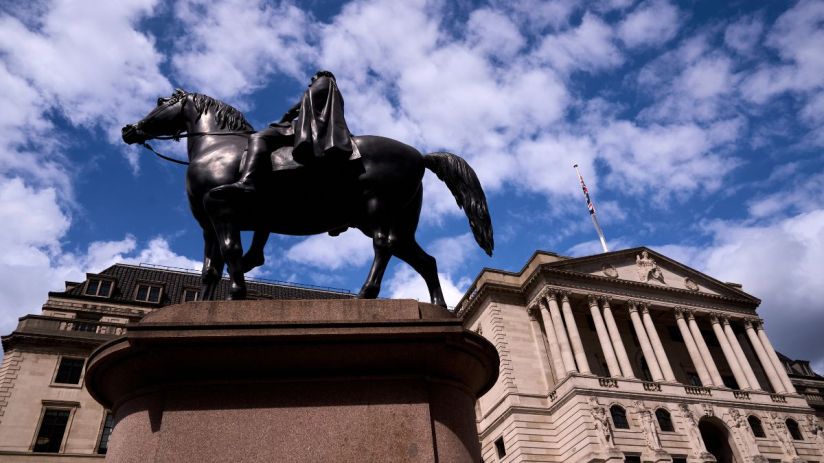 Wellington statue in front of the Bank of England building with a British flag flying under a cloudy sky