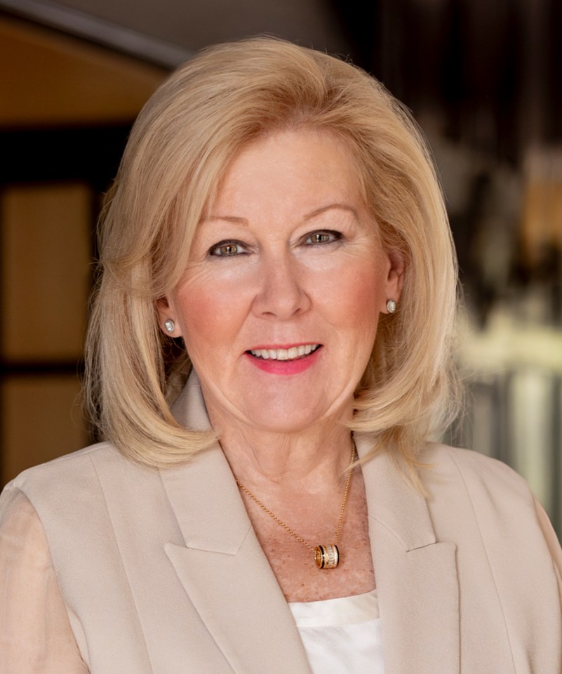 Kate Barton, a blonde woman in a beige blazer and gold necklace, smiling at the camera.