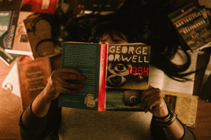 Stack of popular dystopian novels including 1984 and Brave New World on a wooden table, perfect for book enthusiasts.