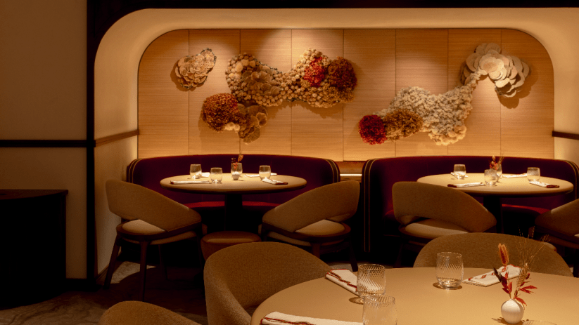 Elegant restaurant interior with round tables, plush burgundy booths, and textured floral wall art