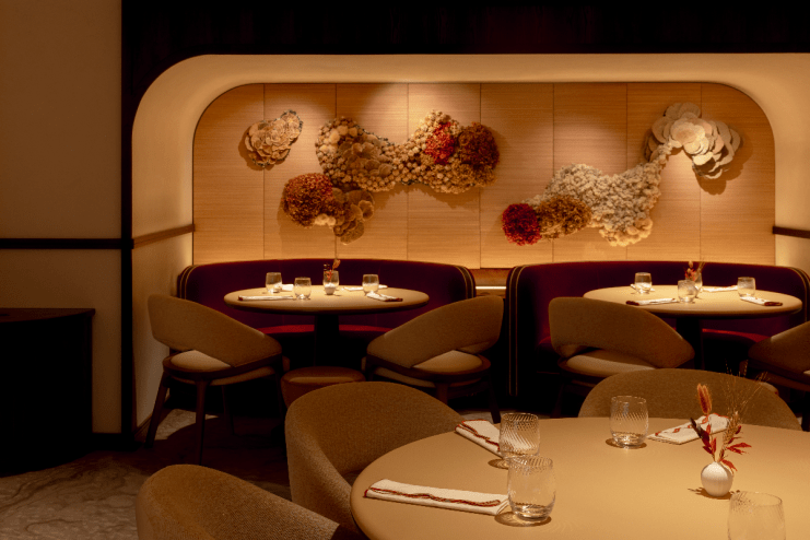 Elegant restaurant interior with round tables, plush burgundy booths, and textured floral wall art