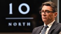 Andy Burnham, Mayor of Greater Manchester, in a suit and glasses, with a 10 NORTH logo in the background