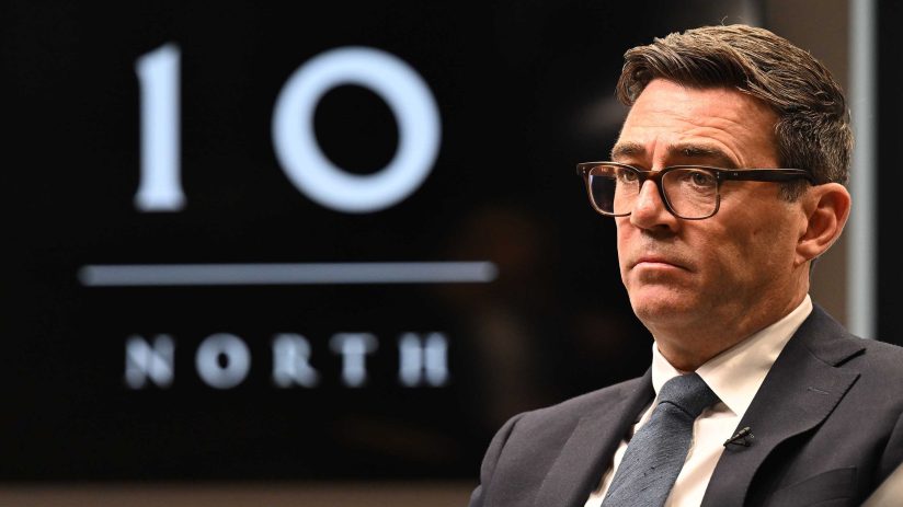 Andy Burnham, Mayor of Greater Manchester, in a suit and glasses, with a 10 NORTH logo in the background