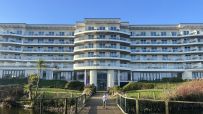 Modern Butlins hotel building with multiple balconies, a path leading to it, and a small pond in the foreground.