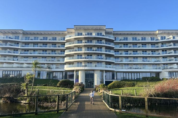 Modern Butlins hotel building with multiple balconies, a path leading to it, and a small pond in the foreground.