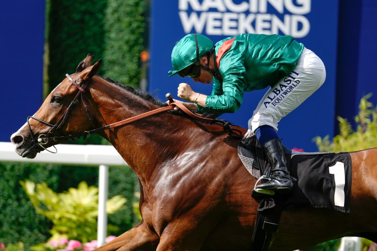 Jockey Calandagan on a brown racehorse, wearing green and white silks, racing past a blue sign with RACING WEEKEND