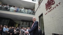 Chancellor Healey speaking at a podium before a crowd, with the HM Treasury sign visible on the brick building.
