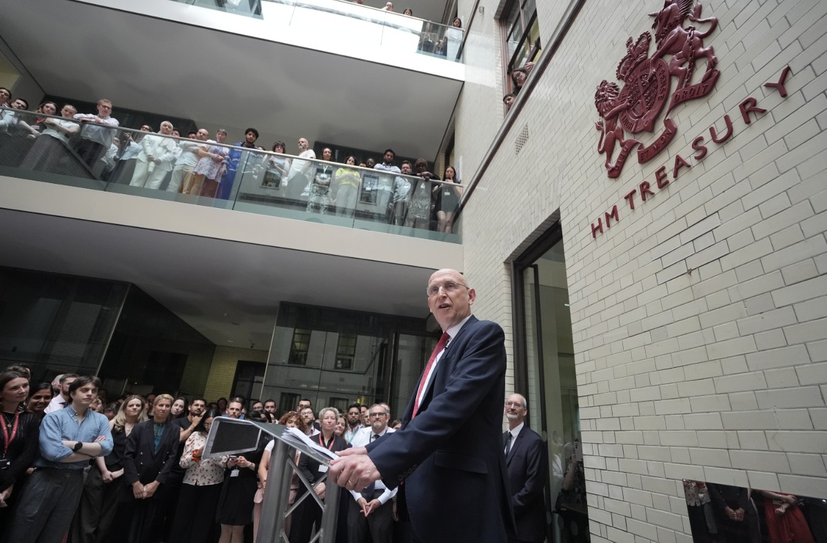 Chancellor Healey speaking at a podium before a crowd, with the HM Treasury sign visible on the brick building.