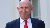 Chancellor John Healey smiling, wearing a navy suit, white shirt, and red tie.