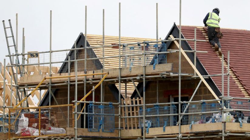 Construction worker on a roof of a new build house, surrounded by scaffolding and building materials.