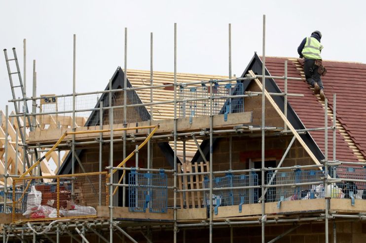Construction worker on a roof of a new build house, surrounded by scaffolding and building materials.