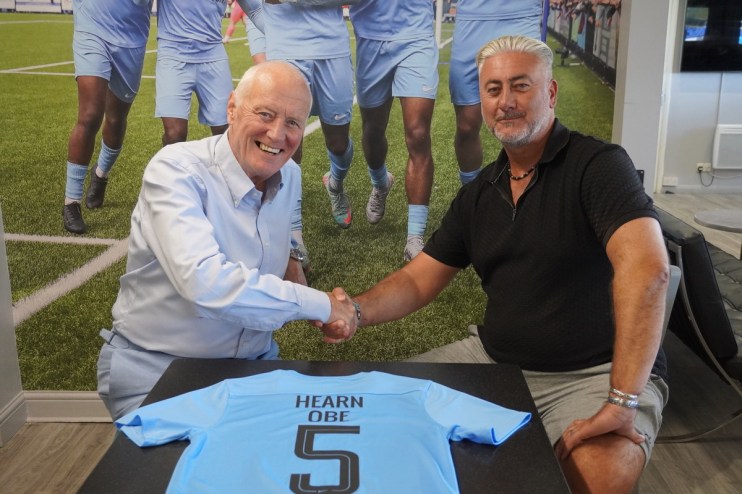 Barry Hearn and a man shaking hands over a light blue football jersey with HEARN OBE 5 printed on it.