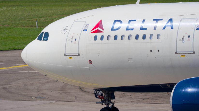 Delta Air Lines aircraft at Heathrow Airport with regulatory compliance signage visible on the runway
