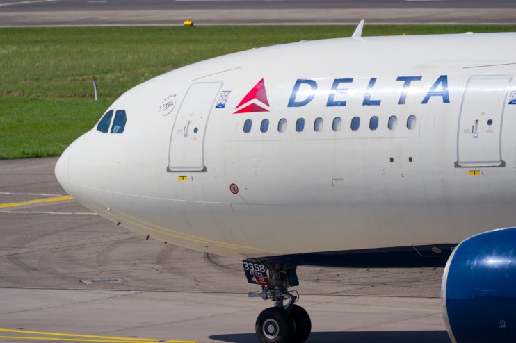 Delta Air Lines aircraft at Heathrow Airport with regulatory compliance signage visible on the runway