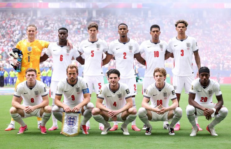 England football team players celebrate on the field with fans in the background during an international match.