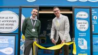 Gavin Peck (right) cuts a yellow ribbon with a man next to him, celebrating the StoryBus launch.