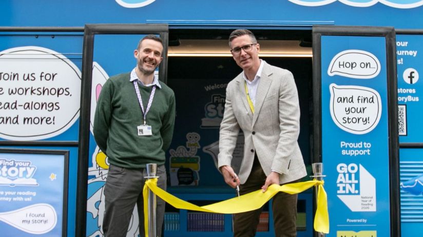Gavin Peck (right) cuts a yellow ribbon with a man next to him, celebrating the StoryBus launch.