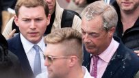 George Cottrell and Nigel Farage engaging in a conversation at a political event, both dressed in formal attire.