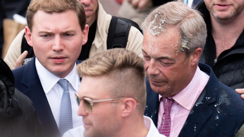 George Cottrell and Nigel Farage engaging in a conversation at a political event, both dressed in formal attire.