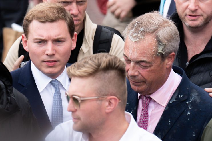 George Cottrell and Nigel Farage engaging in a conversation at a political event, both dressed in formal attire.