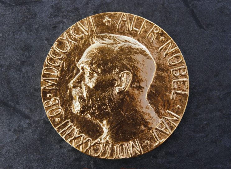 Close-up of a golden Nobel Prize medal featuring Alfred Nobels profile on a dark, textured background.