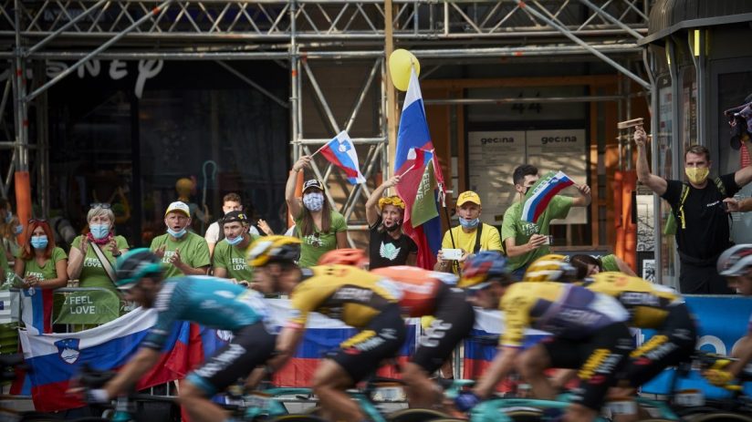 Cycling fans, some in green Feel Slovenia shirts, cheer cyclists with Slovenian flags.