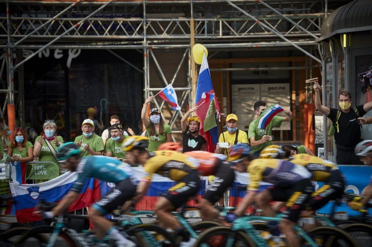 Cycling fans, some in green Feel Slovenia shirts, cheer cyclists with Slovenian flags.