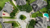 Aerial view of a residential cul-de-sac with houses, green lawns, trees, and a swimming pool