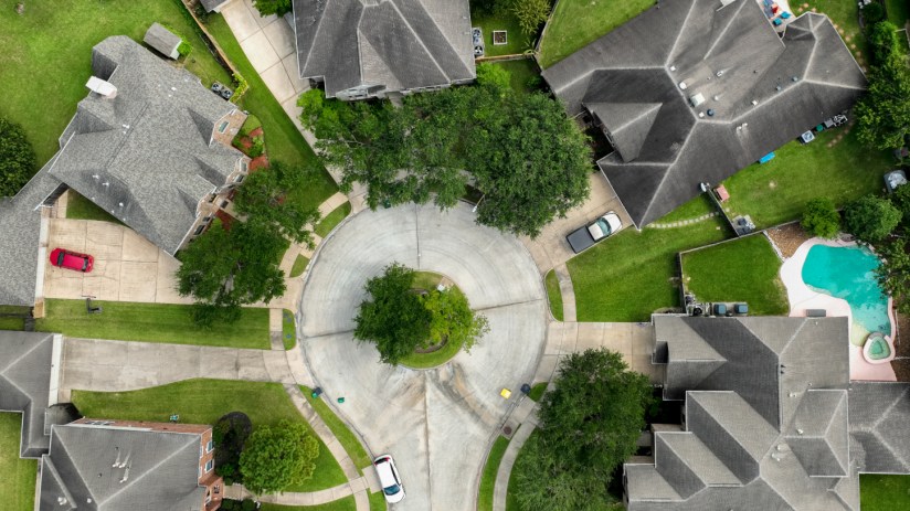 Aerial view of a residential cul-de-sac with houses, green lawns, trees, and a swimming pool