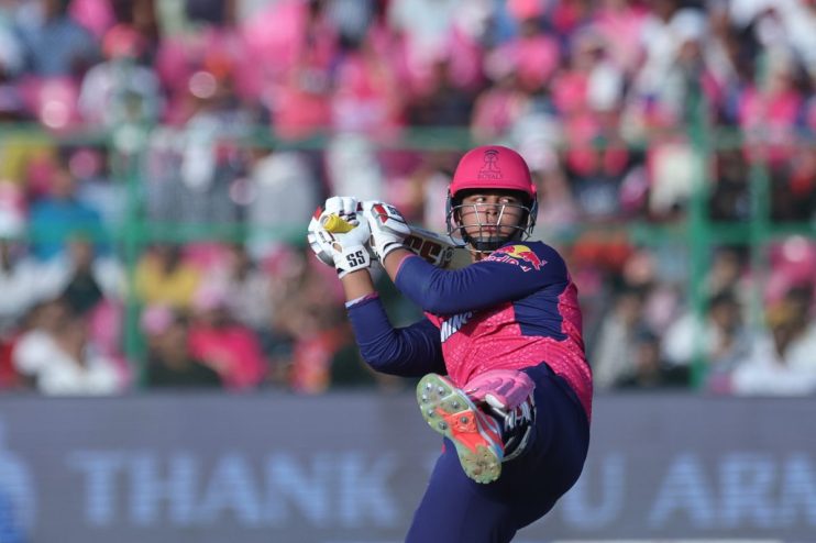 Young cricket player in pink and blue uniform with Rajasthan Royals helmet batting during a match.