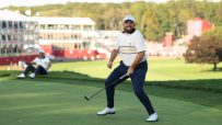 Golfer Shane Lowry celebrating a successful putt on the green with a fist pump and an intense expression.