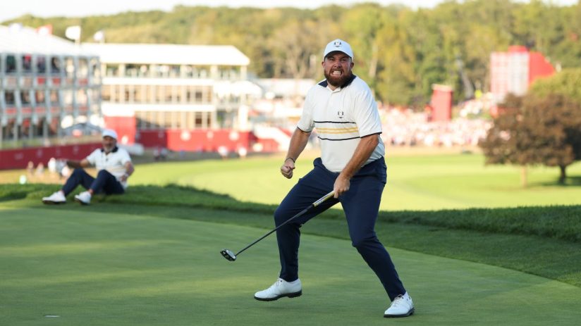 Golfer Shane Lowry celebrating a successful putt on the green with a fist pump and an intense expression.