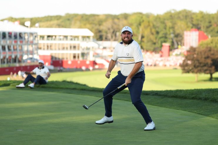 Golfer Shane Lowry celebrating a successful putt on the green with a fist pump and an intense expression.