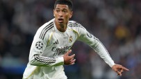 Jude Bellingham in a white Real Madrid jersey with black stripes, looking focused on the field during a match.