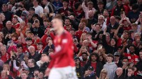 Excited football fans in a stadium, many wearing red shirts, cheering and holding up phones.