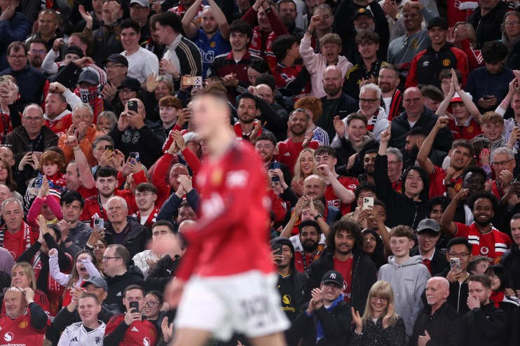 Excited football fans in a stadium, many wearing red shirts, cheering and holding up phones.
