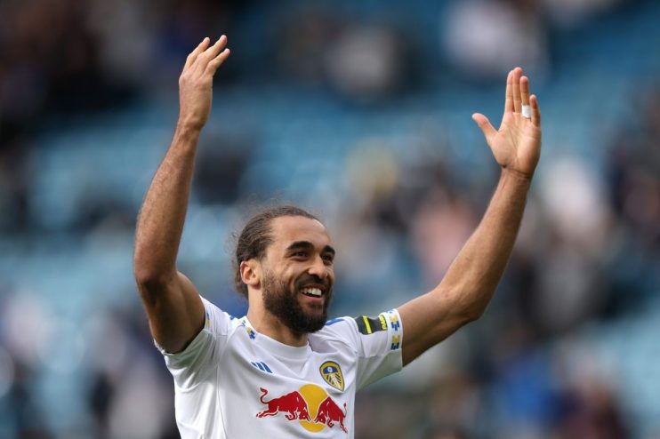Happy male soccer player with beard and long hair in white uniform raising arms, smiling