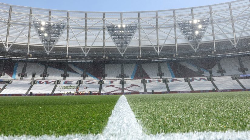 Football pitch with a white line, stadium seats, and bright lights under a clear sky.