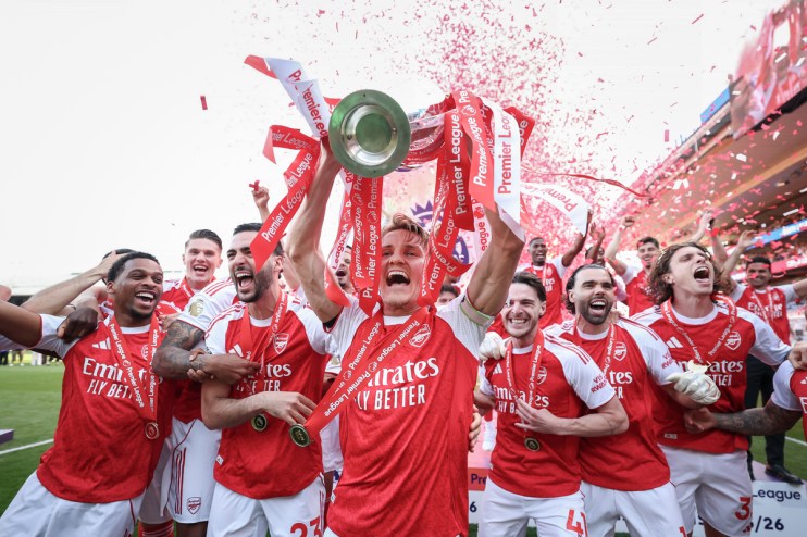 Arsenal players celebrate with the Premier League trophy and confetti raining down, cheering on the field.