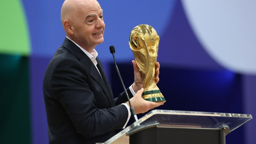 Gianni Infantino holding the FIFA World Cup trophy while speaking at a podium.