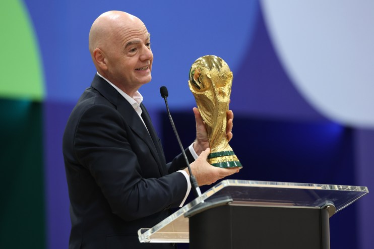 Gianni Infantino holding the FIFA World Cup trophy while speaking at a podium.
