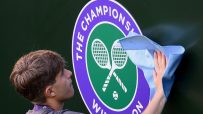 A person cleaning the Wimbledon Championships logo, featuring crossed tennis rackets and a ball.