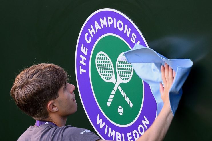 A person cleaning the Wimbledon Championships logo, featuring crossed tennis rackets and a ball.