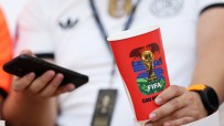 Person holding a red FIFA World Cup branded cup and a smartphone, wearing a white shirt and watch