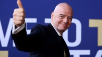 Gianni Infantino smiling and giving a thumbs up, wearing a suit against a blue and white background.