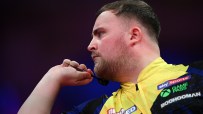 A male darts player in a yellow and blue shirt holding a dart, focused on his throw.